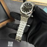 Stainless steel Audemars Piguet wristwatch with a black textured dial held by a black-gloved hand in a display setting