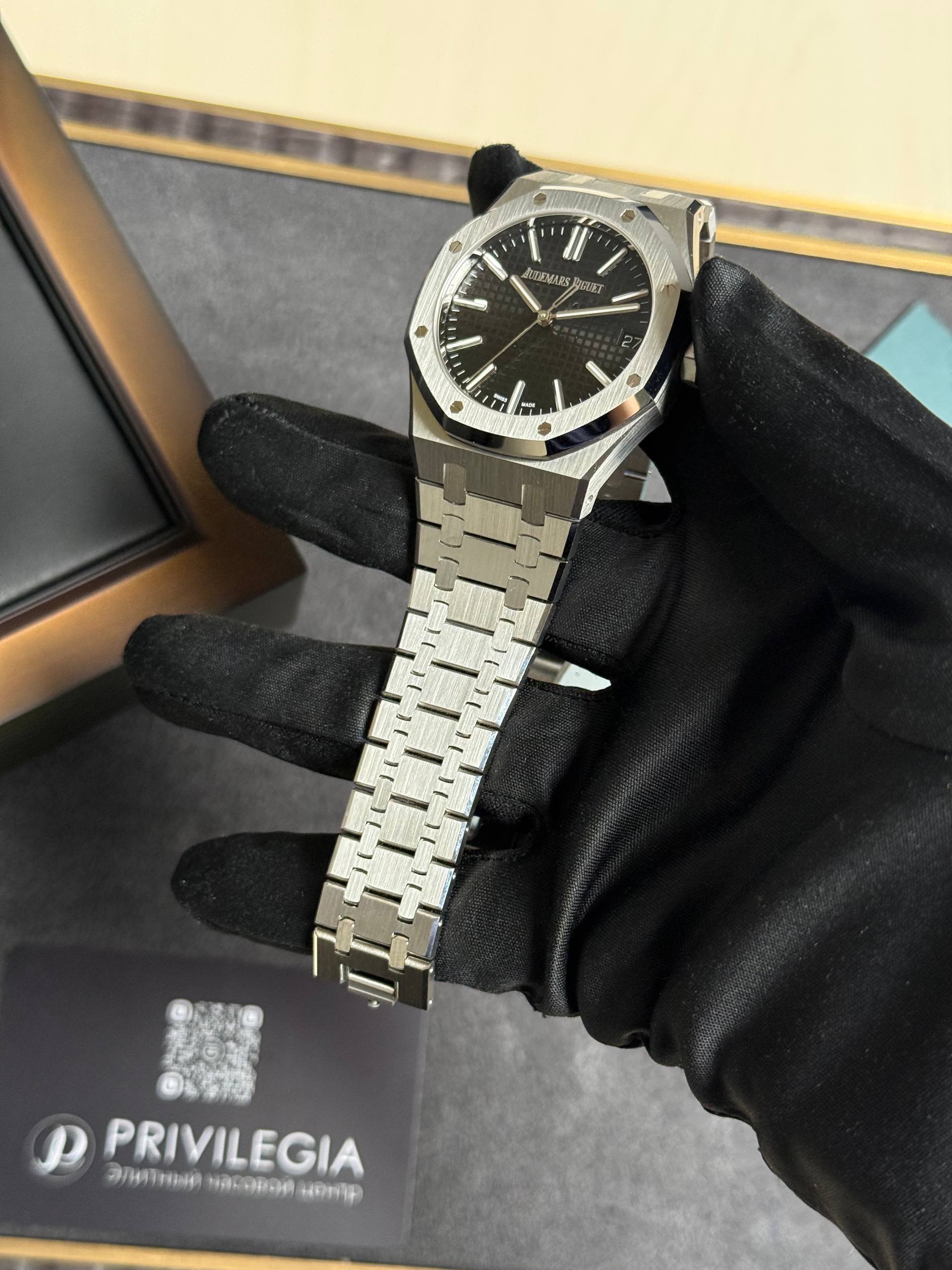 Stainless steel Audemars Piguet wristwatch with a black textured dial held by a black-gloved hand in a display setting