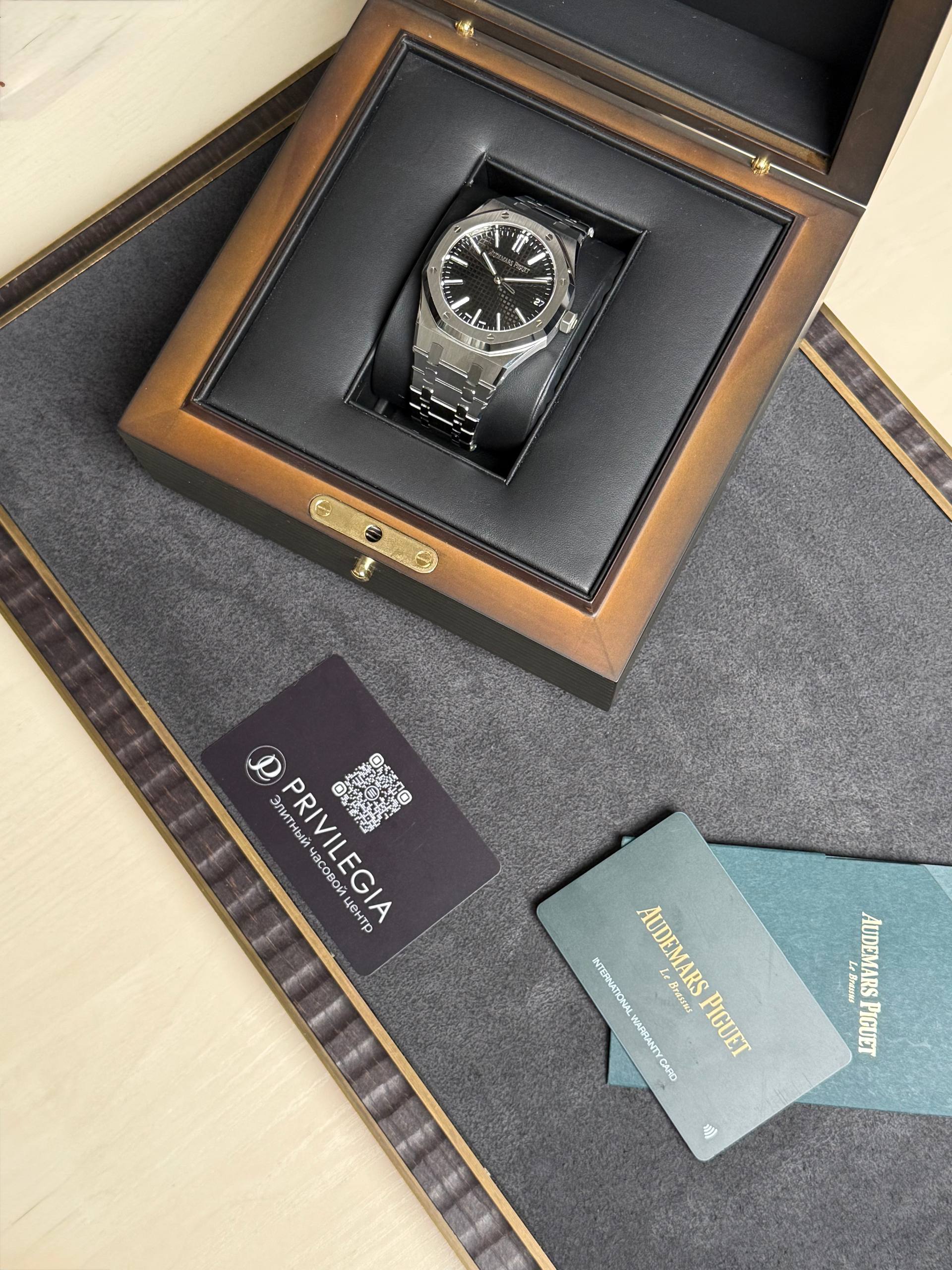 Stainless steel wristwatch in a black-lined wooden presentation box, with the Audemars Piguet logo on the black dial.