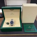 Rolex Oyster Perpetual Datejust in green presentation box with blue dial and diamond bezel, displayed on a store counter.