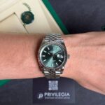 Close-up of a stainless steel Rolex Datejust on a wrist with a green dial, resting on a dark Privilegia box.