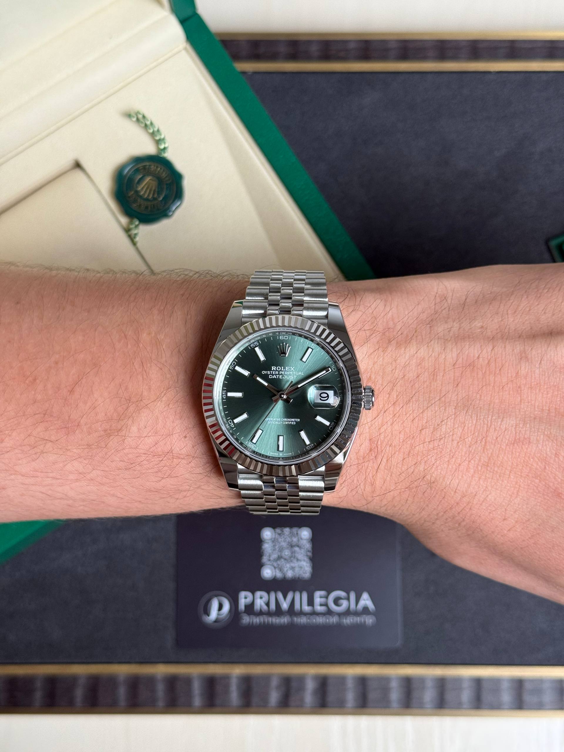 Close-up of a stainless steel Rolex Datejust on a wrist with a green dial, resting on a dark Privilegia box.