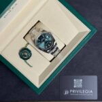 Rolex stainless steel wristwatch with green dial in its beige presentation box, with green seal tag nearby.