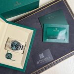 Rolex Datejust in stainless steel presented in a green and beige gift box with a green cardholder and warranty tag nearby