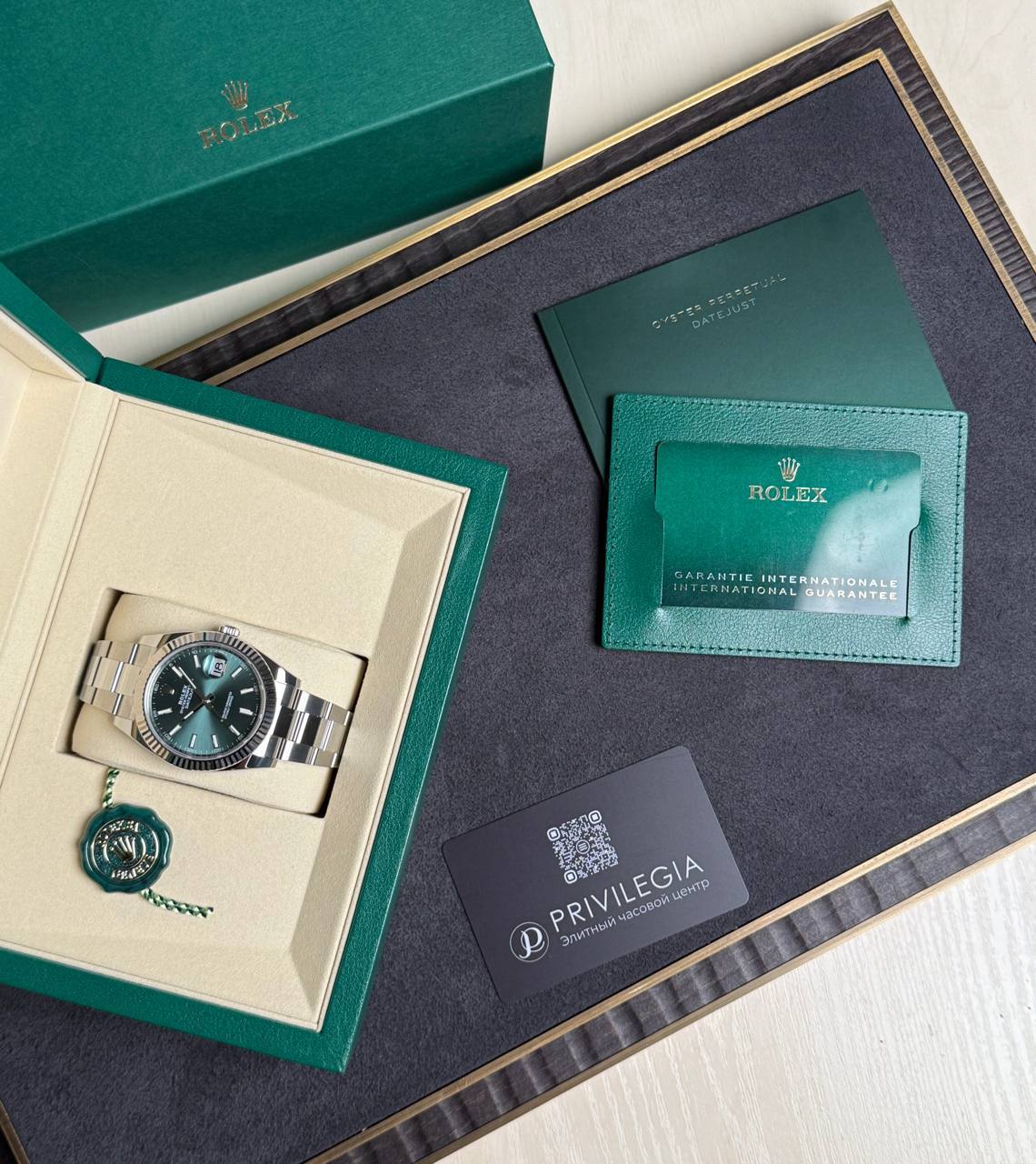 Rolex Datejust in stainless steel presented in a green and beige gift box with a green cardholder and warranty tag nearby