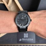 Black Hublot automatic wristwatch on a hairy wrist, date shows 22, with a metal bracelet and dark dial in focus.