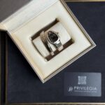 Gold and silver wristwatch with diamond-studded bezel in an open jewelry box, cream lining and a Privilegia card nearby
