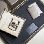 Bulgari watch and matching bracelet in an open beige presentation box with cream padding and boxed accessories nearby.