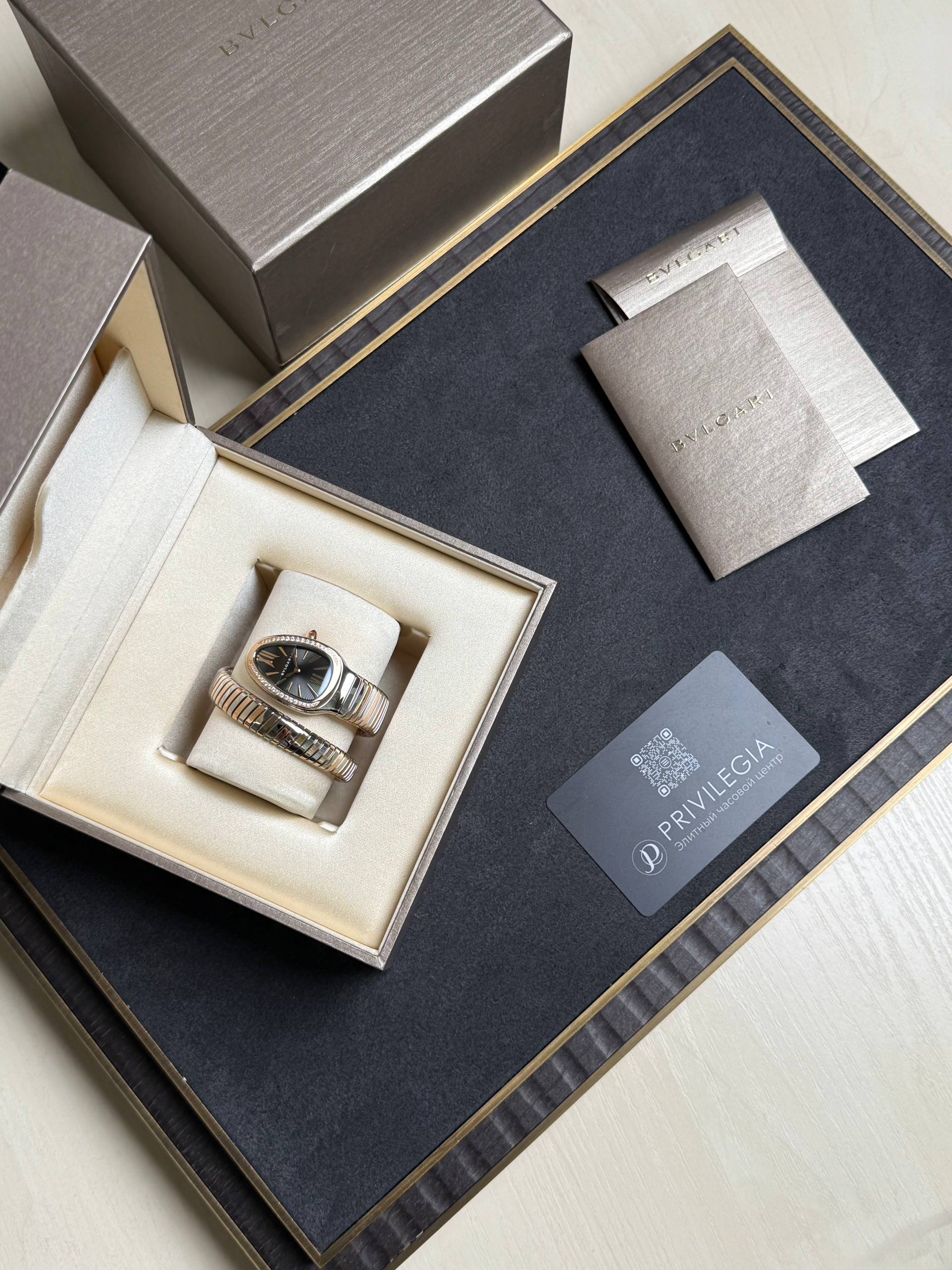 Bulgari watch and matching bracelet in an open beige presentation box with cream padding and boxed accessories nearby.