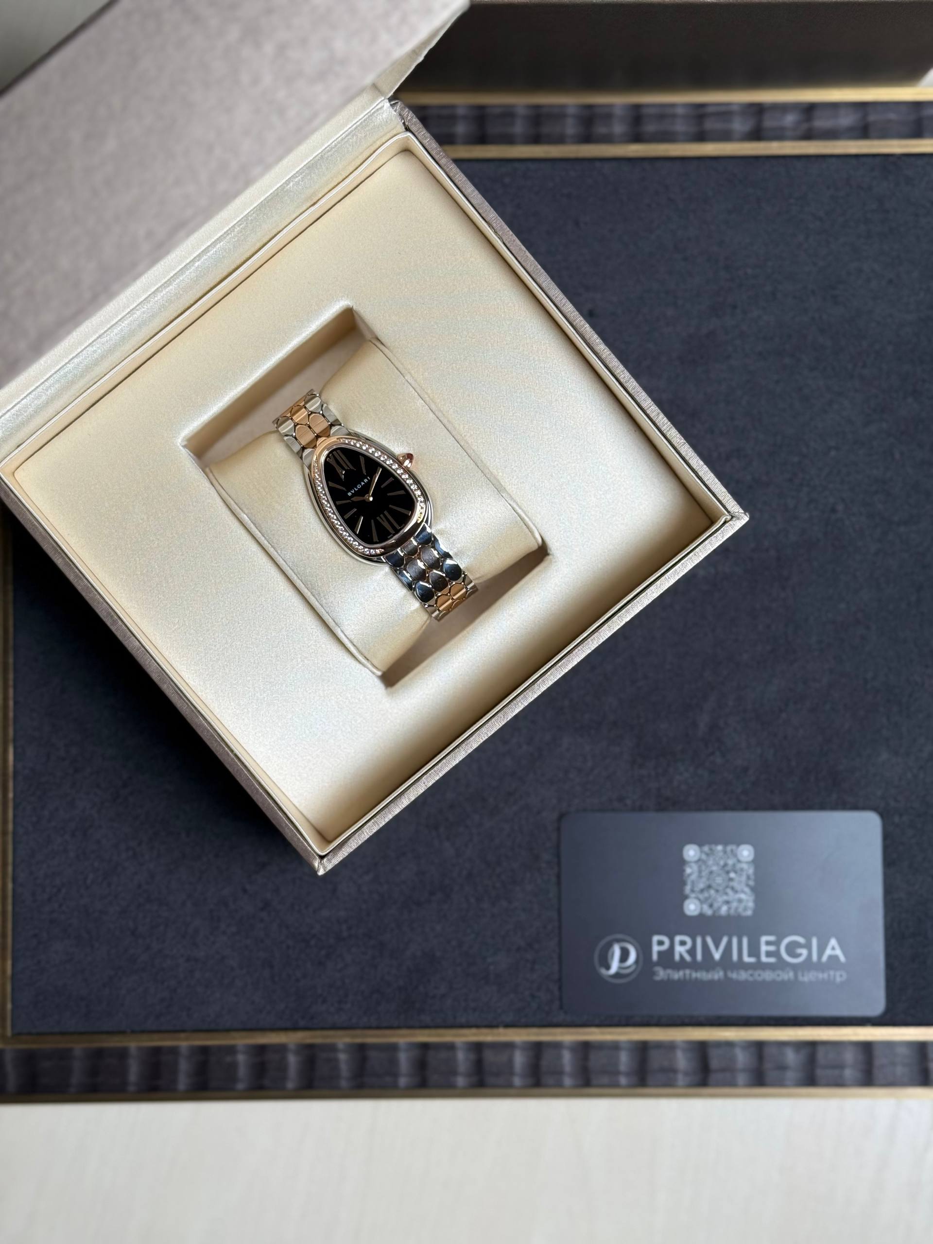 Two-tone wristwatch with a black dial placed in a cream jewelry box, next to a Privilege card in a black sleeve.