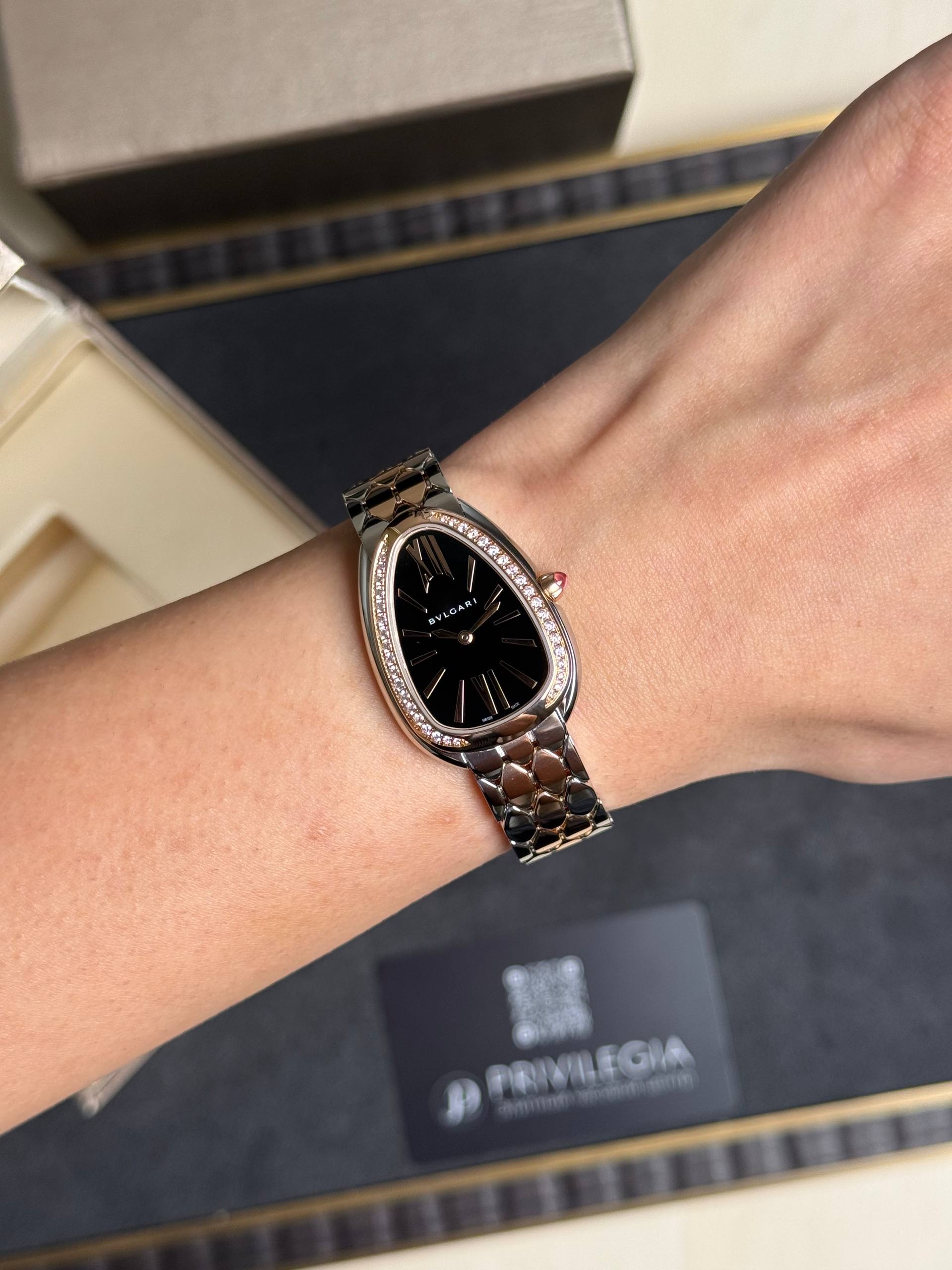 Woman wearing a silver Bulgari wristwatch with a black dial and diamond-studded bezel on the wrist.