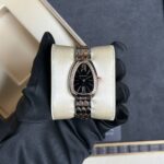 Two-tone BVLGARI wristwatch with diamond bezel resting on a cream cushion, held by a gloved hand.