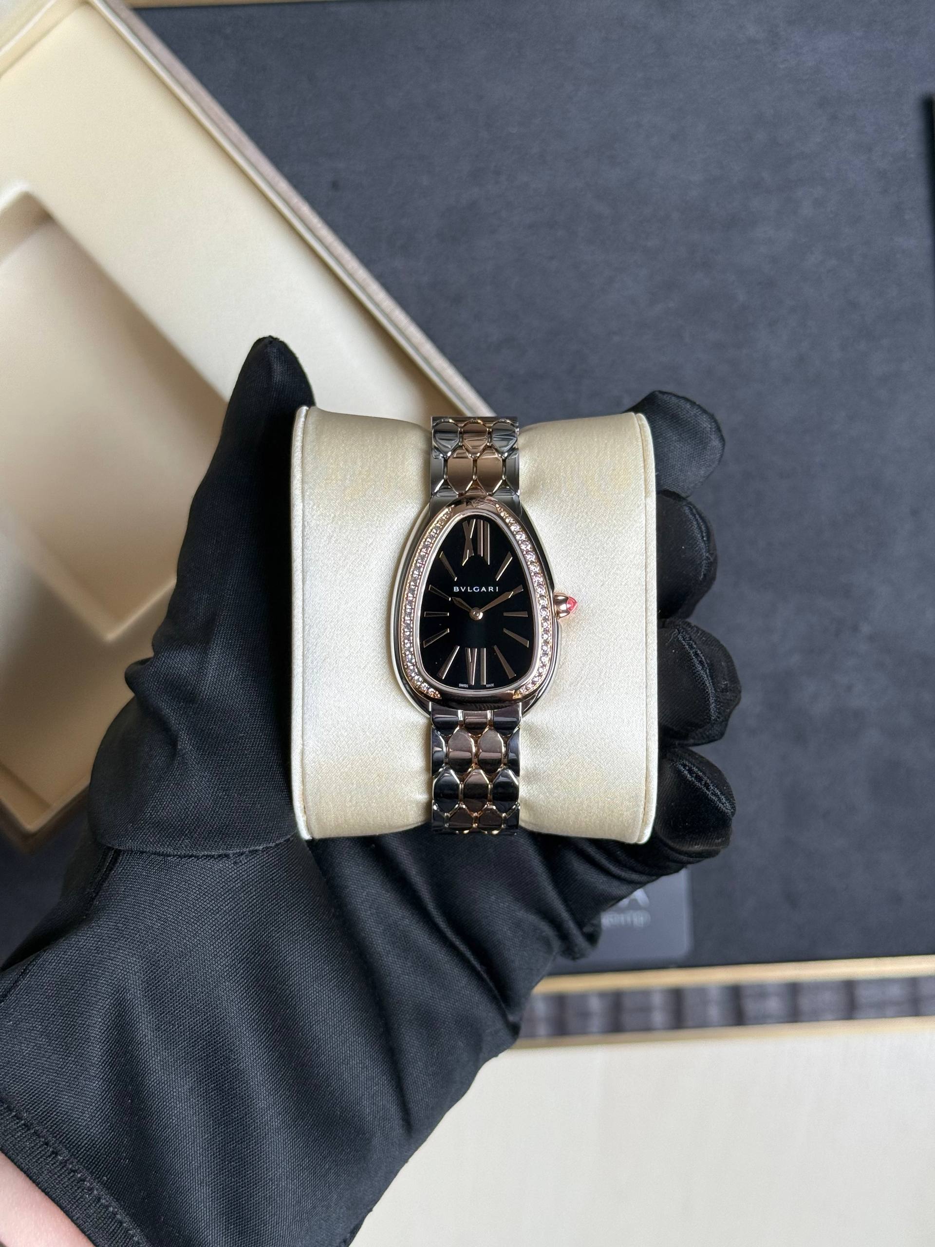 Two-tone BVLGARI wristwatch with diamond bezel resting on a cream cushion, held by a gloved hand.