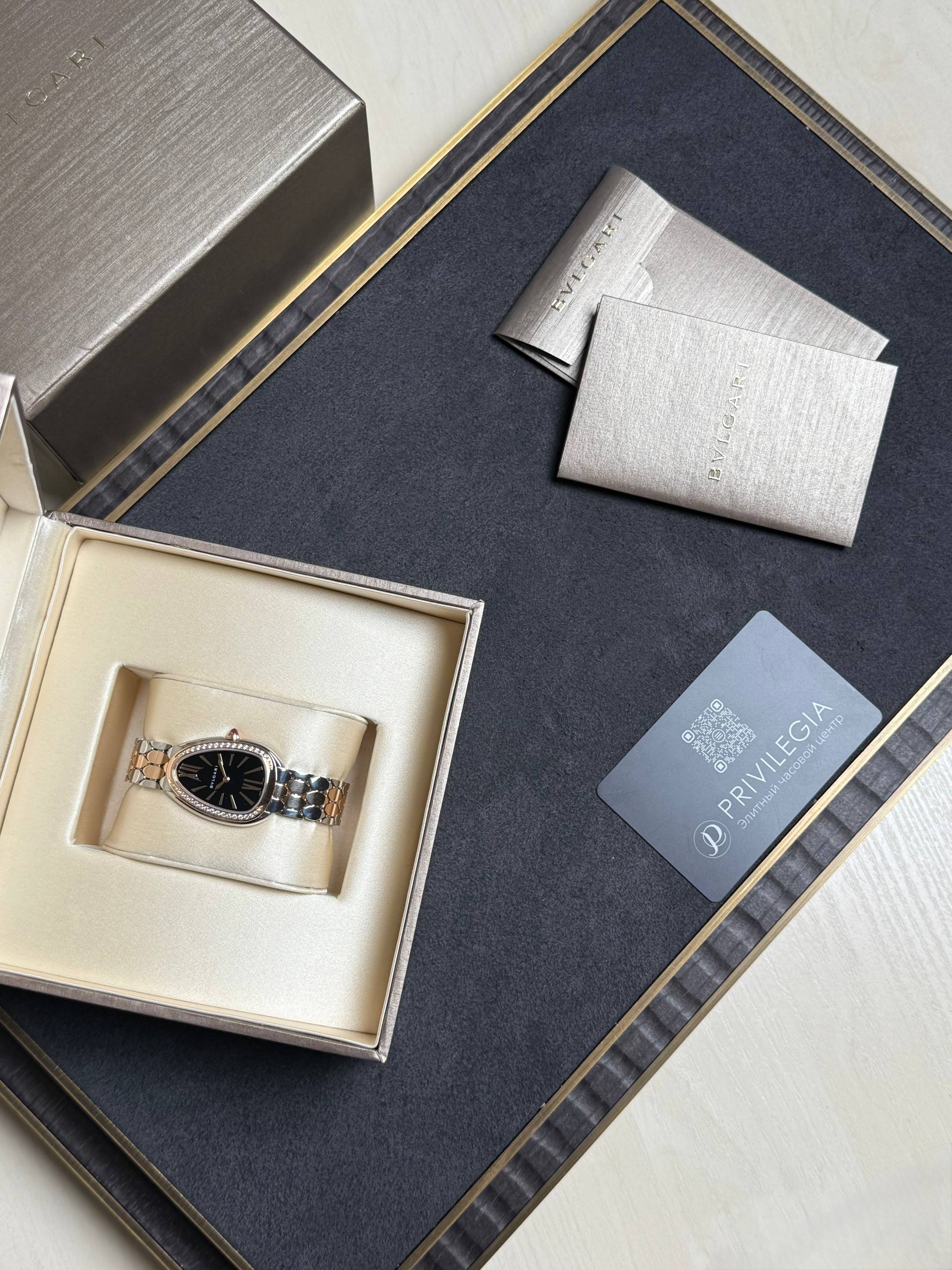Two-tone BVLGARI wristwatch with a black dial in a cream display box, surrounded by elegant packaging.