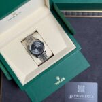 Rolex watch displayed in an open green box with cream interior and metal bracelet, next to Privilegia card