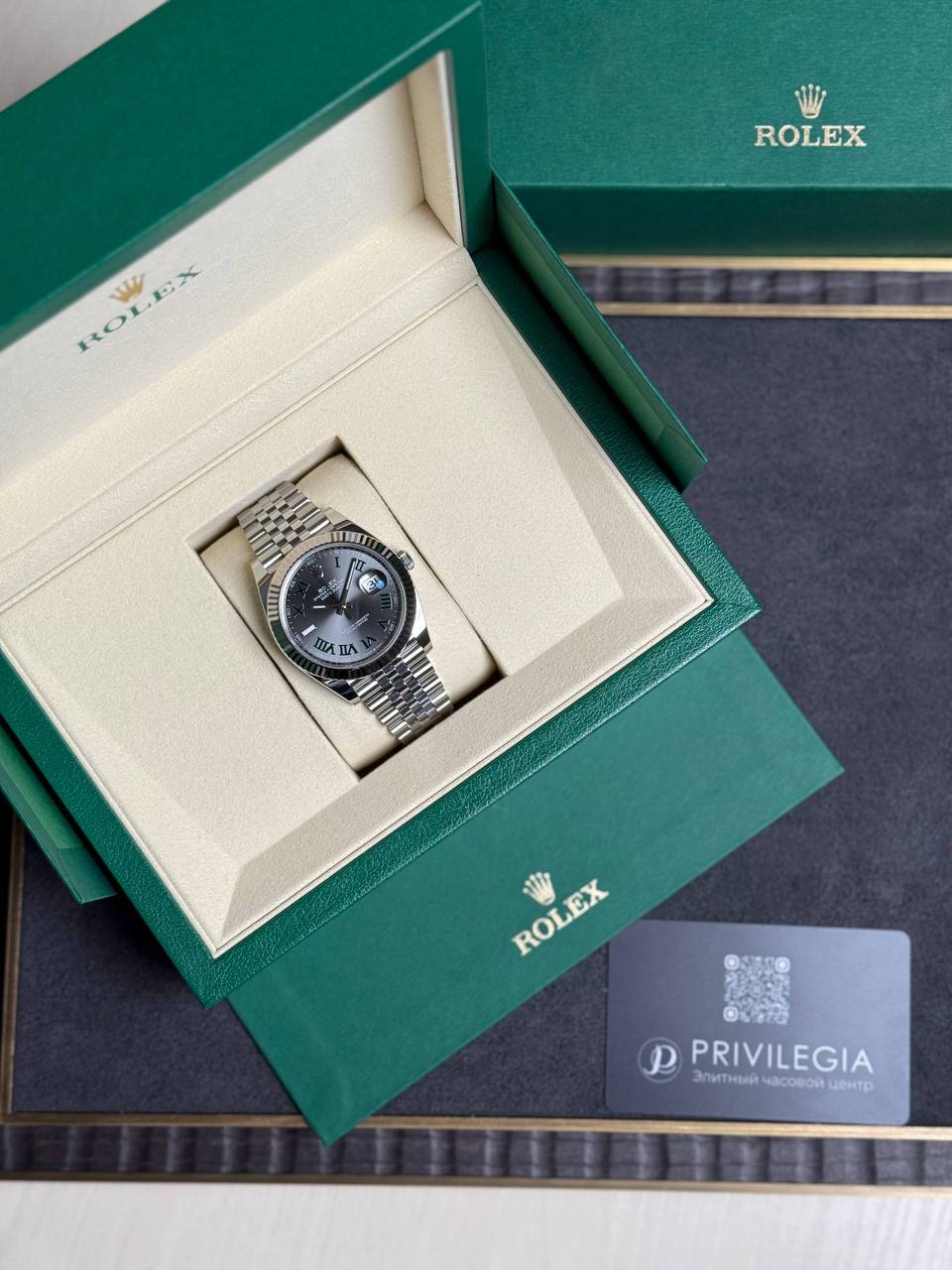 Rolex watch displayed in an open green box with cream interior and metal bracelet, next to Privilegia card