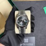 Rolex Datejust on a cushion with a gray dial and green Roman numerals, stainless steel bracelet in a display box.
