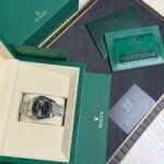 Rolex watch nestled in a cream interior of a green presentation box with accompanying warranty papers and booklets nearby.