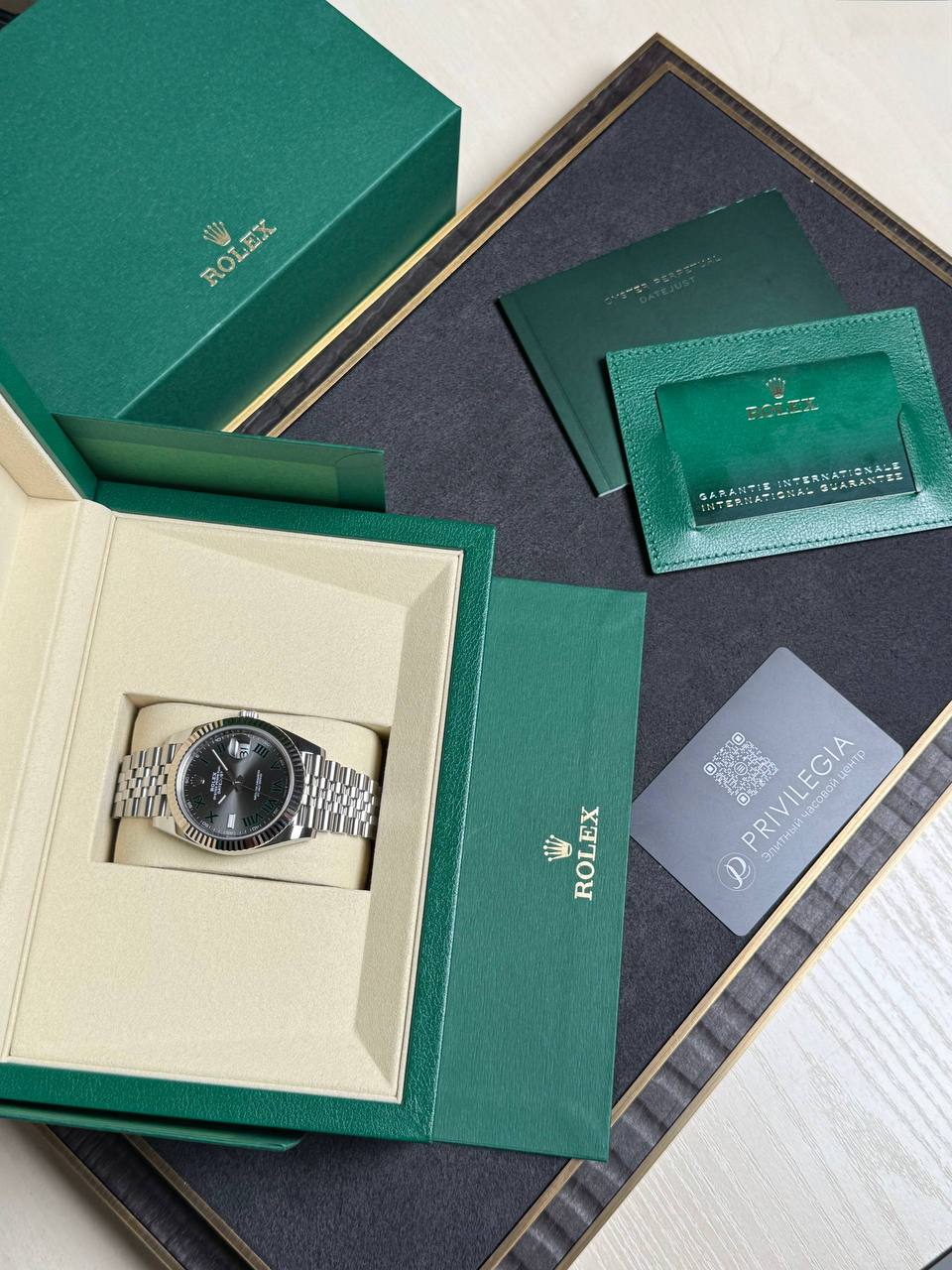 Rolex watch nestled in a cream interior of a green presentation box with accompanying warranty papers and booklets nearby.