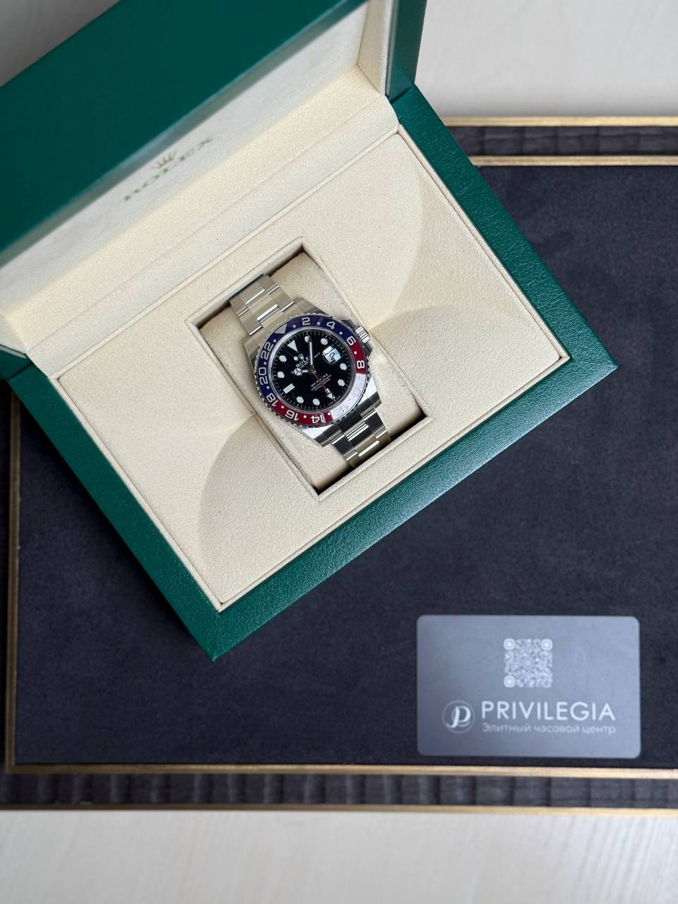 Rolex GMT-Master II in a green presentation box on a beige insert, with a Privilegia card nearby.