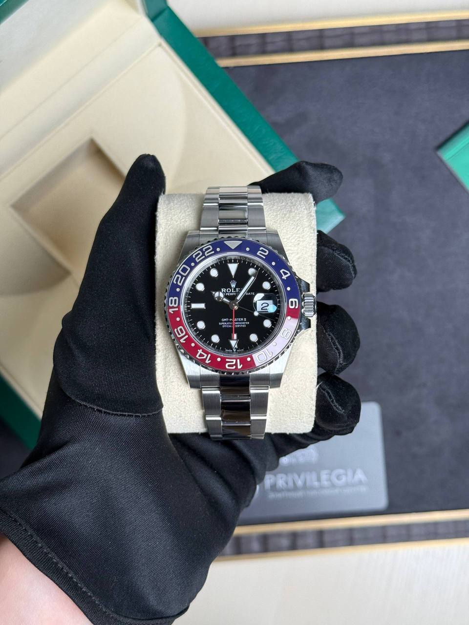 Stainless steel Rolex GMT‑Master II on a display pillow, blue‑red bezel and black dial under a gloved hand pocketed in a box.