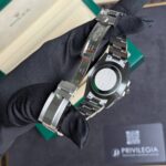 Stainless steel Rolex watch held by a gloved hand, with a green Rolex box open in the background.