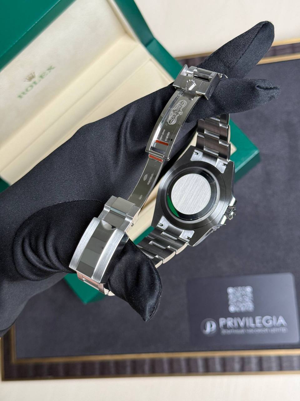 Stainless steel Rolex watch held by a gloved hand, with a green Rolex box open in the background.