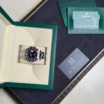 Rolex GMT-Master II with red-blue bezel in an open green box, surrounded by warranty card and green booklet.