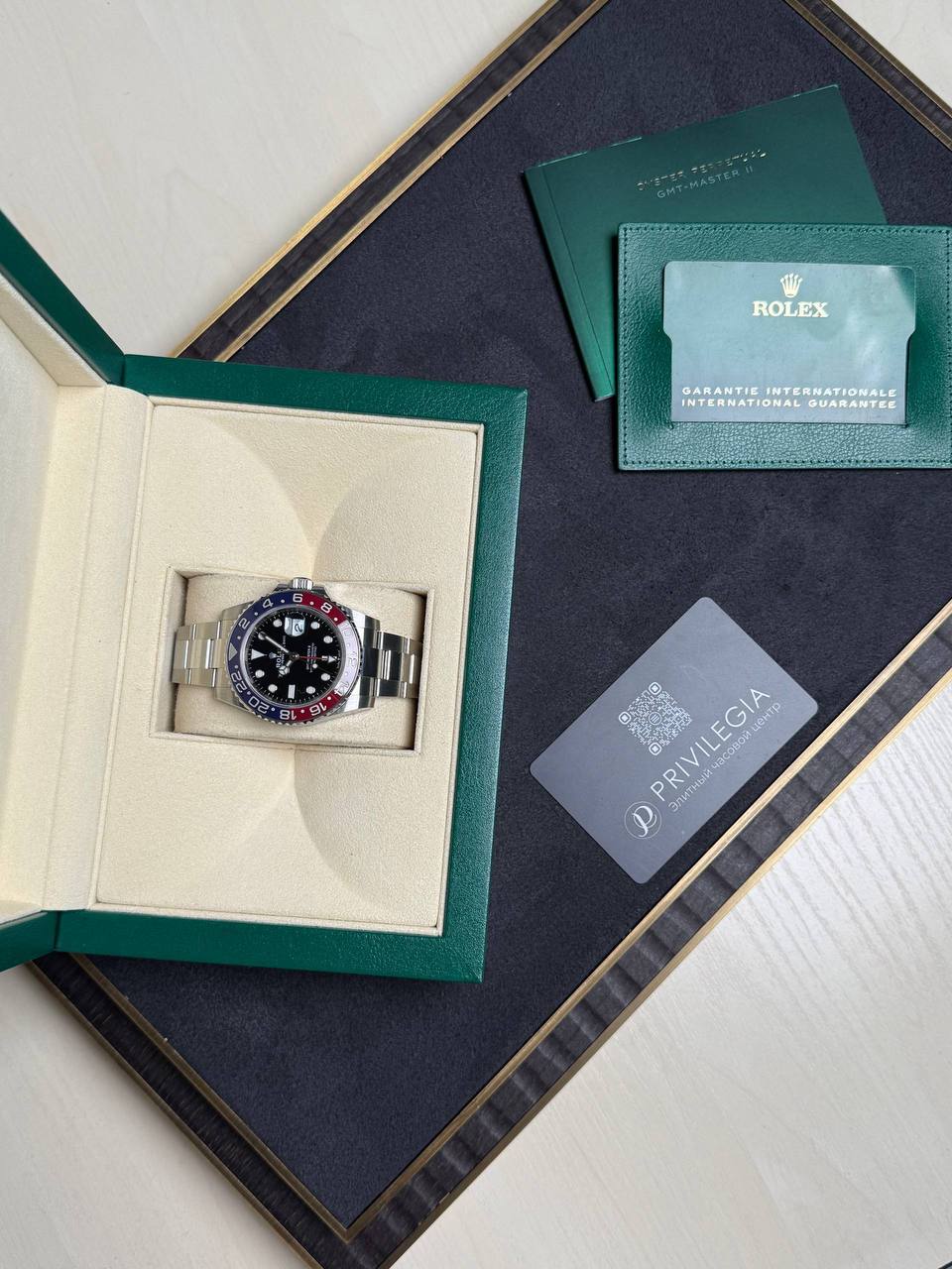 Rolex GMT-Master II with red-blue bezel in an open green box, surrounded by warranty card and green booklet.