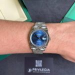 Silver Rolex wristwatch with blue dial and Jubilee bracelet on a forearm inside a green presentation box