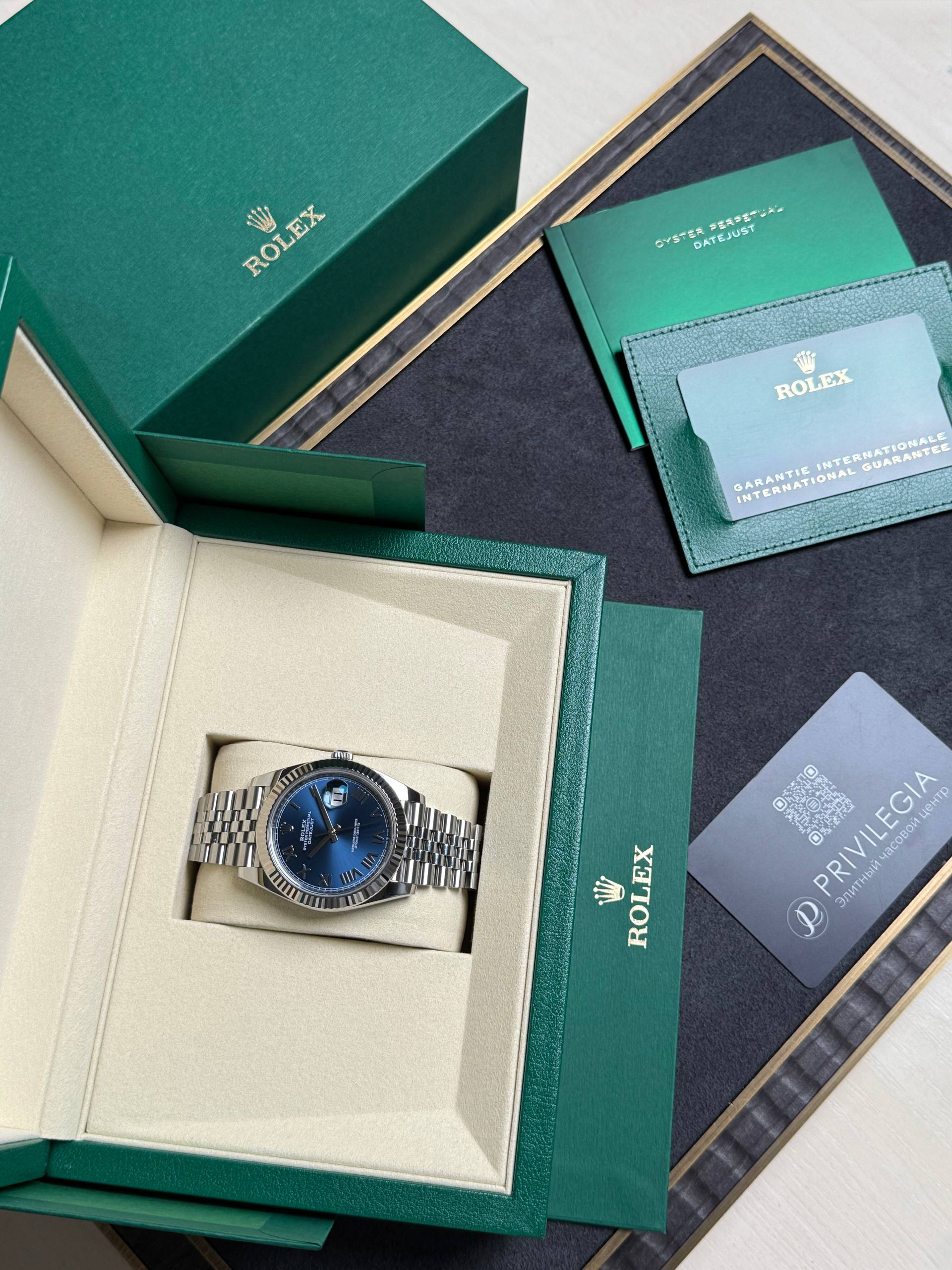 Rolex watch in beige inner box with green outer packaging and accompanying certificates and cardholders nearby