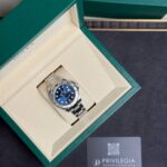 Rolex watch in its green presentation box with cream lining, blue dial and silver bracelet visible.