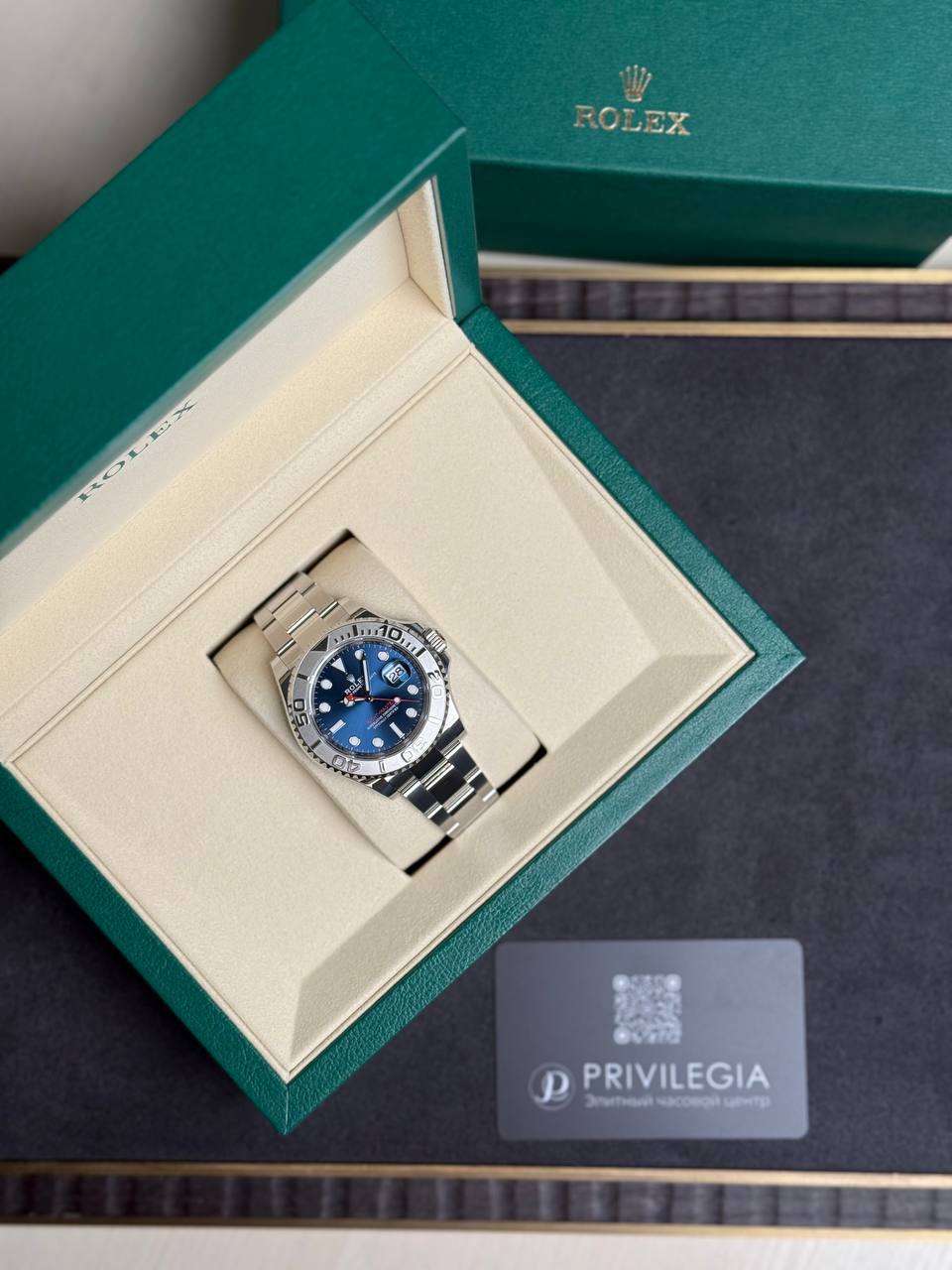 Rolex watch in its green presentation box with cream lining, blue dial and silver bracelet visible.