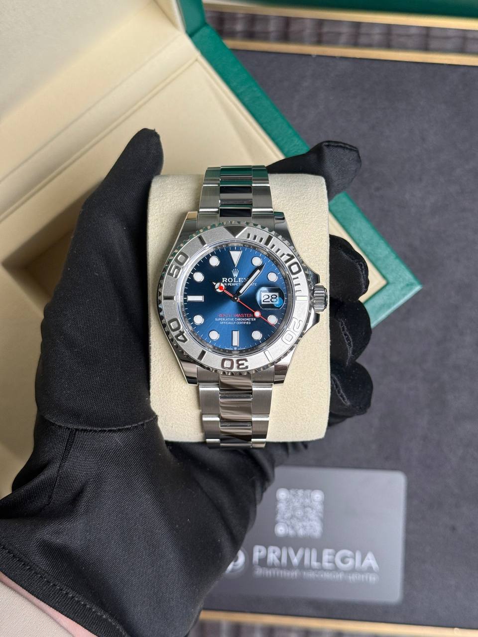 Rolex stainless steel dive watch with blue dial and date window, held in a gloved hand on a beige cushion.