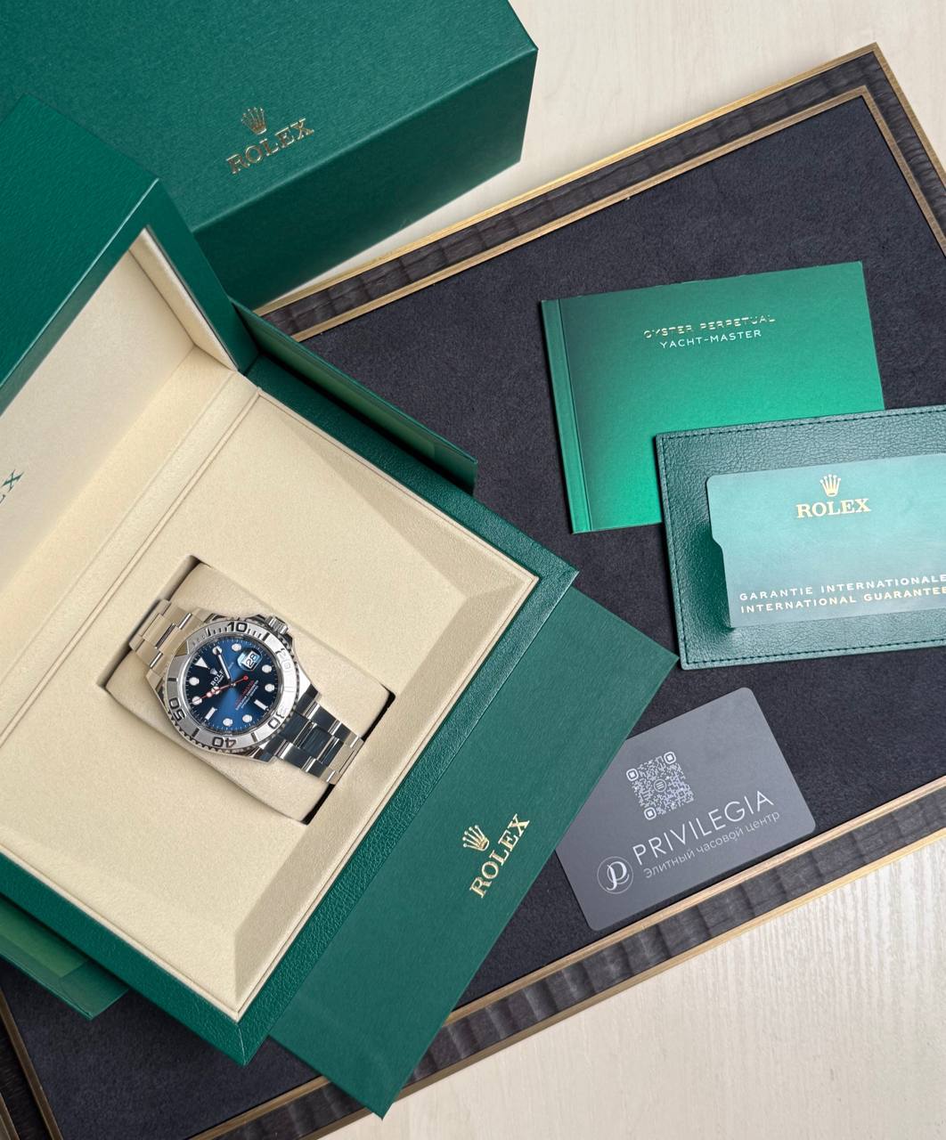 Green Rolex box opened to reveal a stainless steel watch in a beige insert, with warranty cards and booklets nearby.