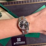 Two-tone Rolex Datejust watch on the wrist with a green Rolex box in the background.