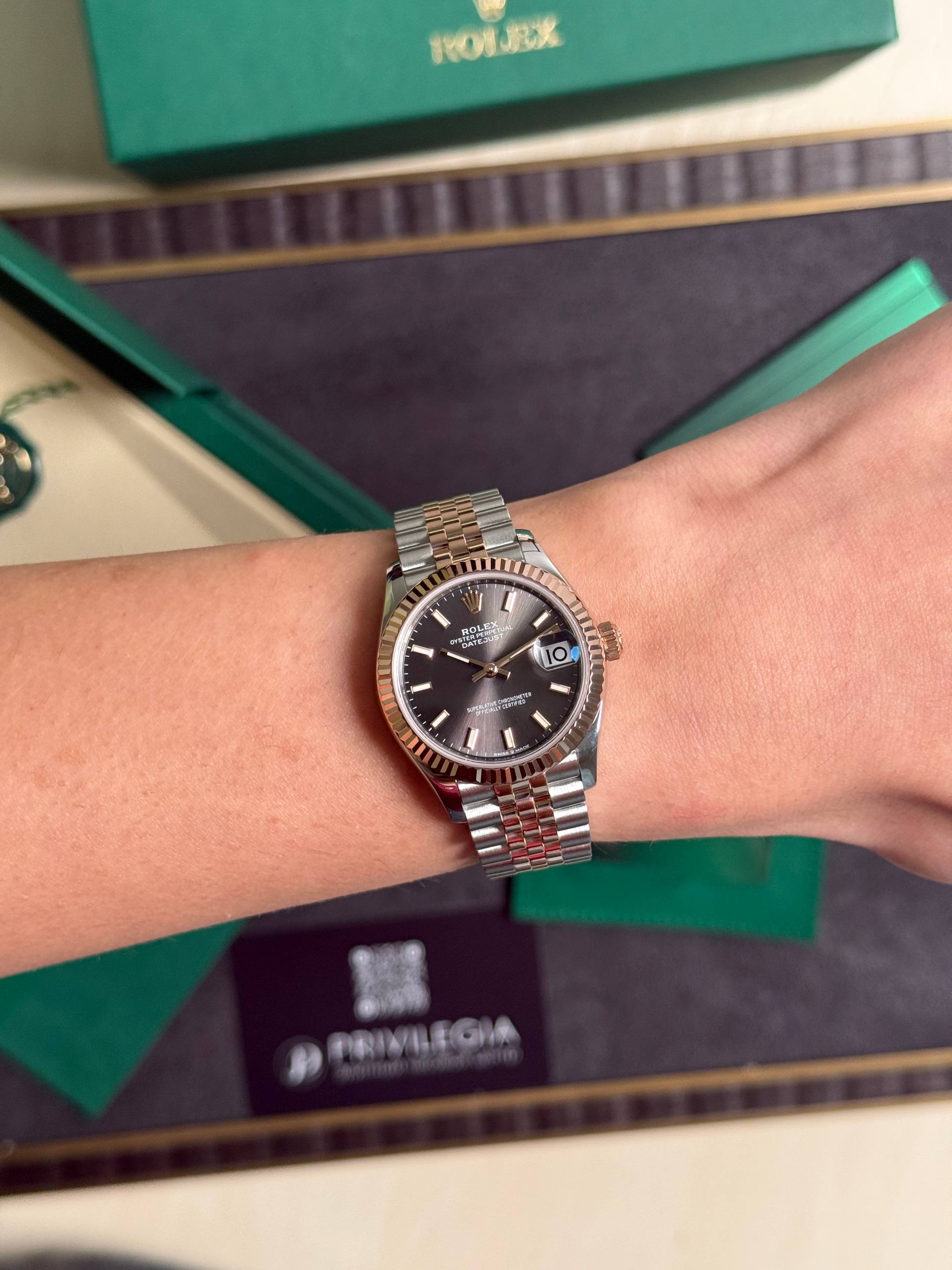 Two-tone Rolex Datejust watch on the wrist with a green Rolex box in the background.