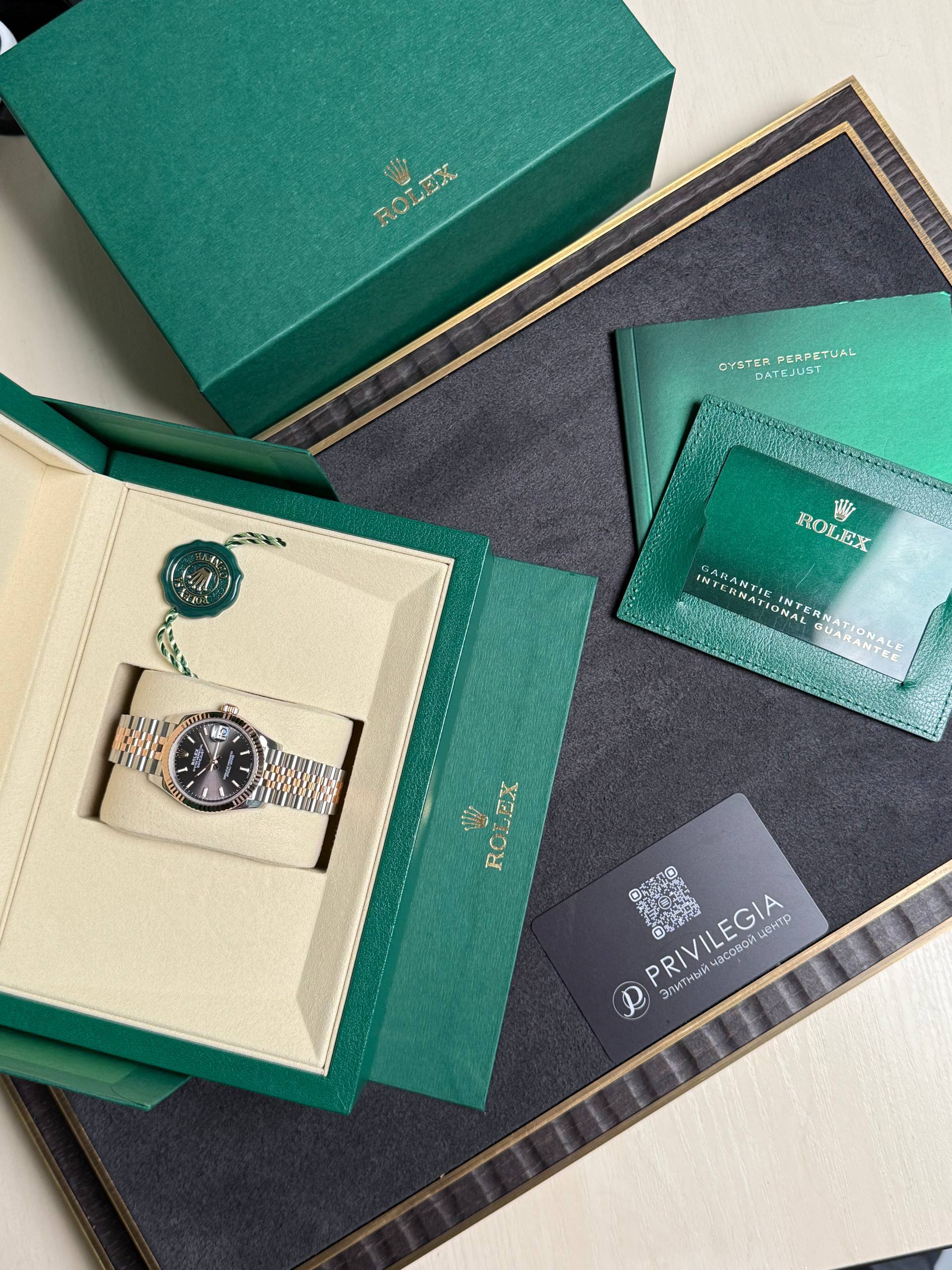 Green Rolex presentation box open to reveal a two-tone Rolex watch in a cream insert with green warranty cards nearby.