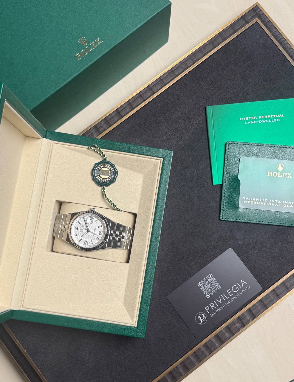 Rolex watch in open green box with beige interior, alongside green card and warranty papers on a black surface