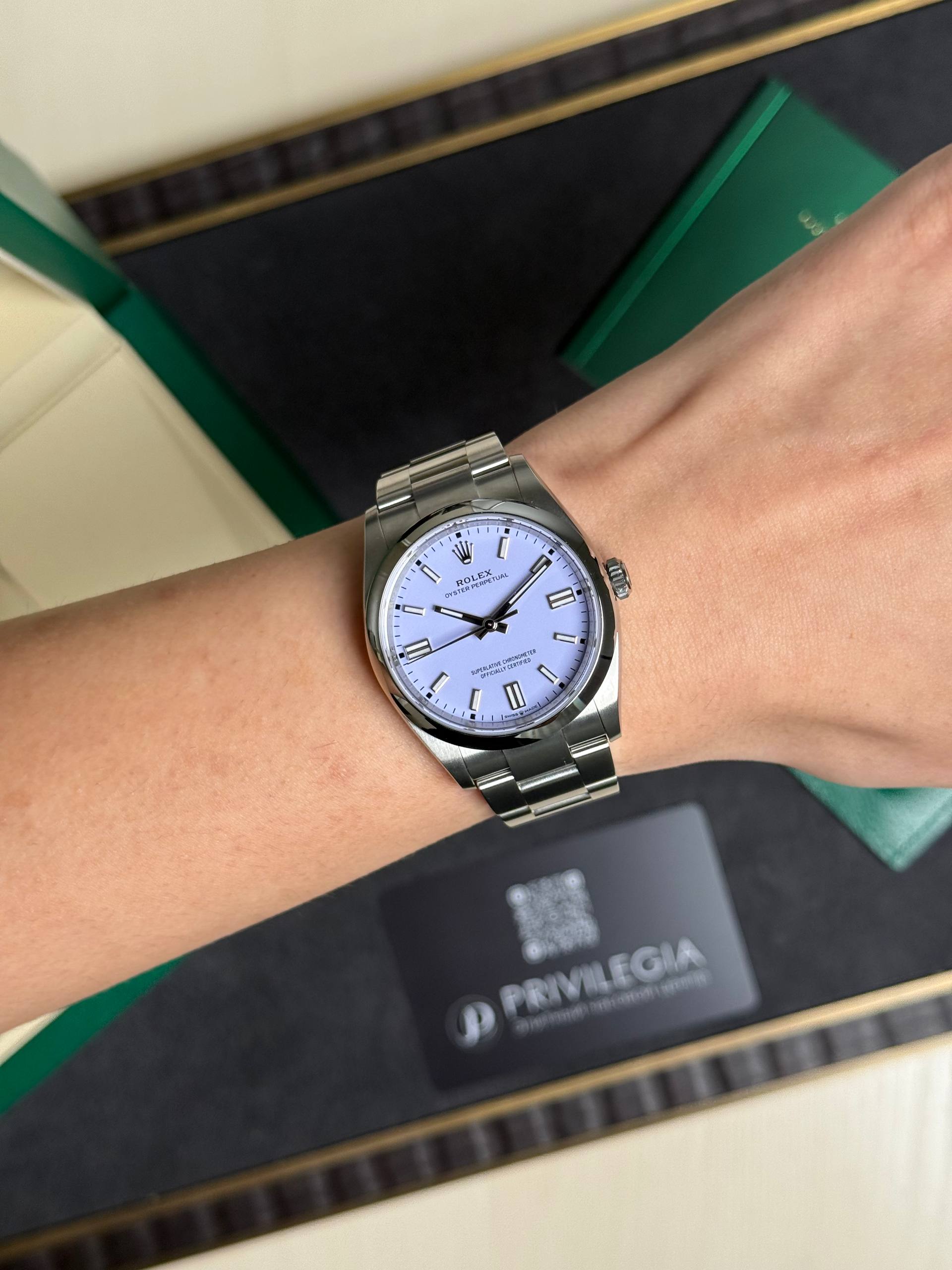 Wrist wearing a silver Rolex Oyster Perpetual with a light blue dial and metal bracelet