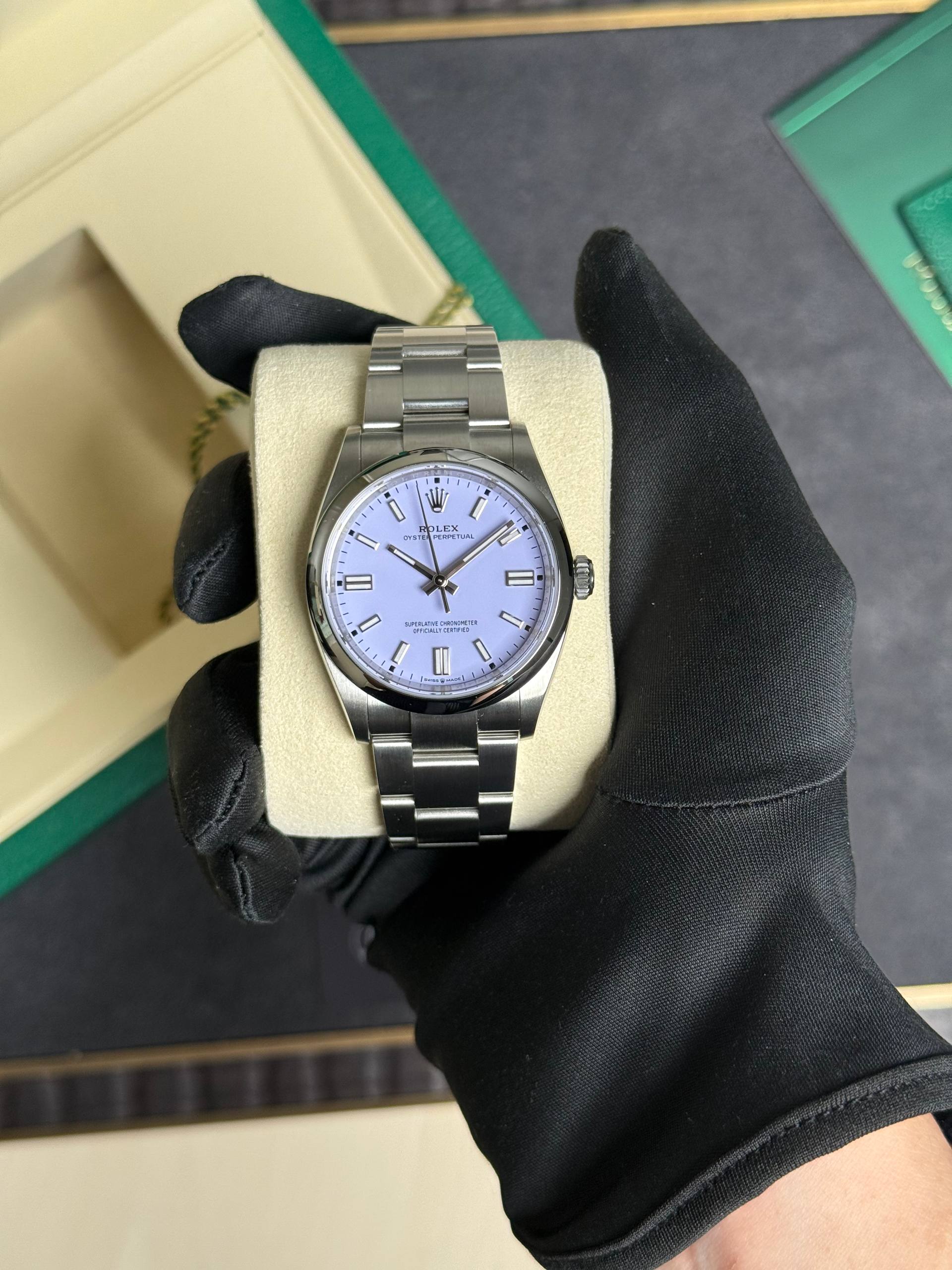 Stainless steel Rolex watch on a beige cushion, held by a gloved hand with a lavender dial showing timepieces.