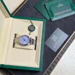 Rolex wristwatch in an open beige display box with a green outer cover, plus green warranty card and documentation nearby.
