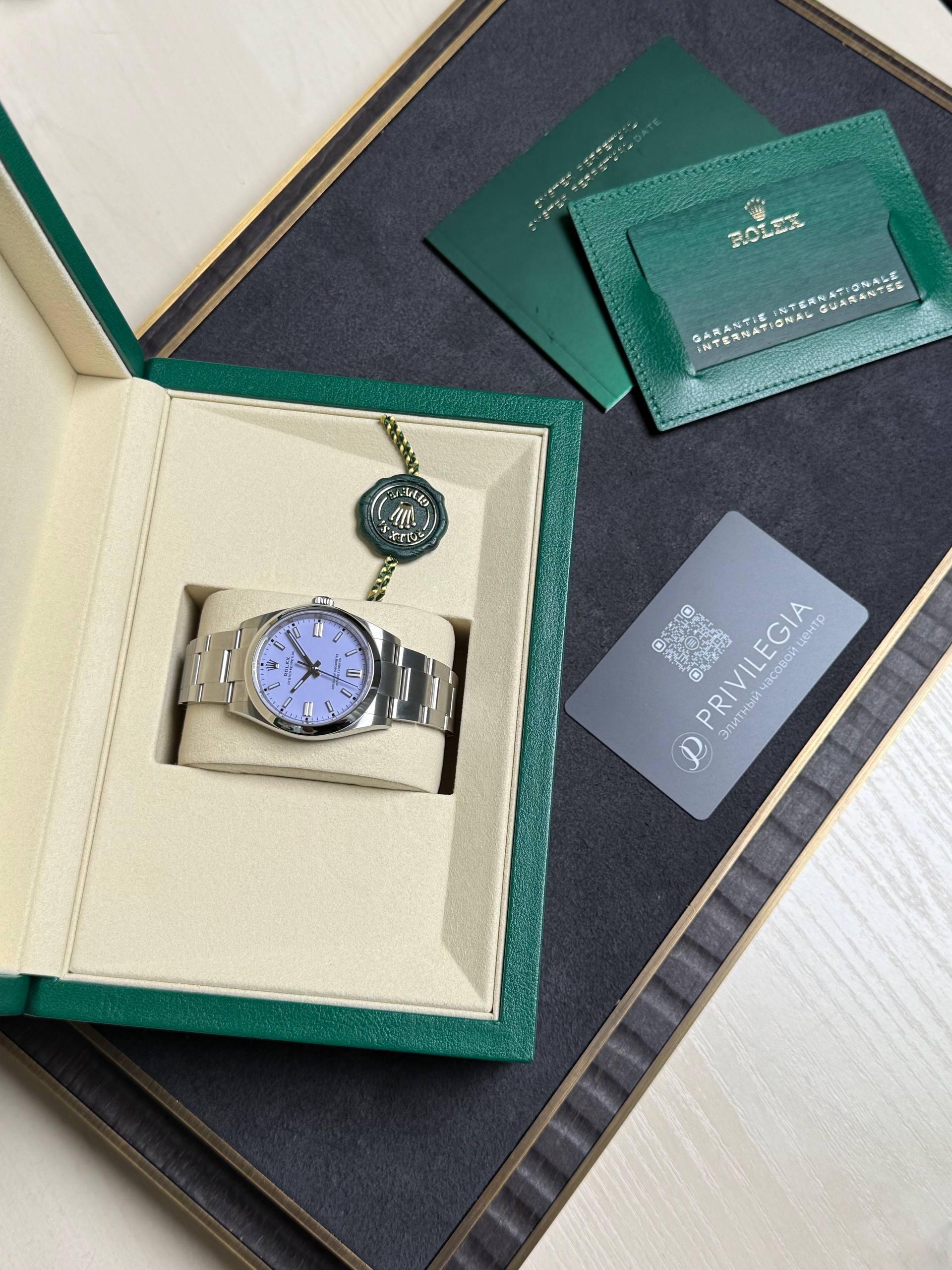 Rolex wristwatch in an open beige display box with a green outer cover, plus green warranty card and documentation nearby.