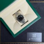 Rolex stainless steel wristwatch with a black dial and date window displayed in an open green presentation box.