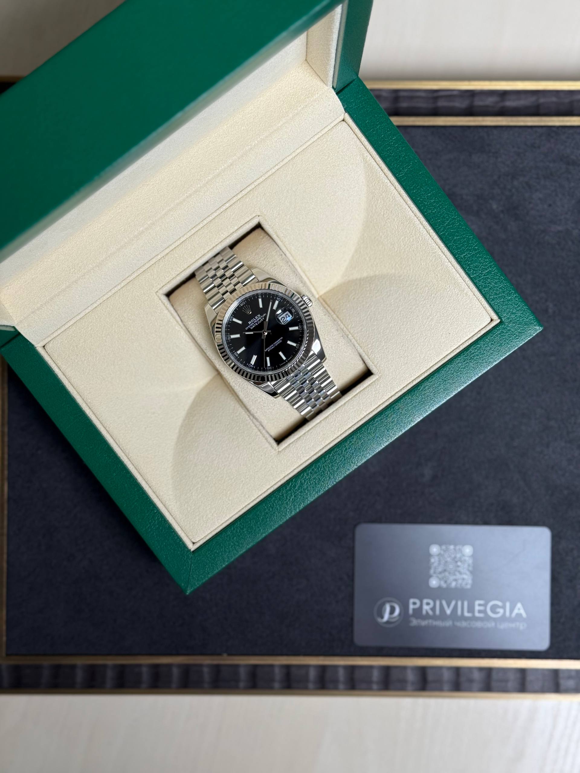 Rolex stainless steel wristwatch with a black dial and date window displayed in an open green presentation box.