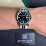Close-up of a stainless steel Rolex watch on a wrist, featuring a black dial, fluted bezel, and Jubilee bracelet.