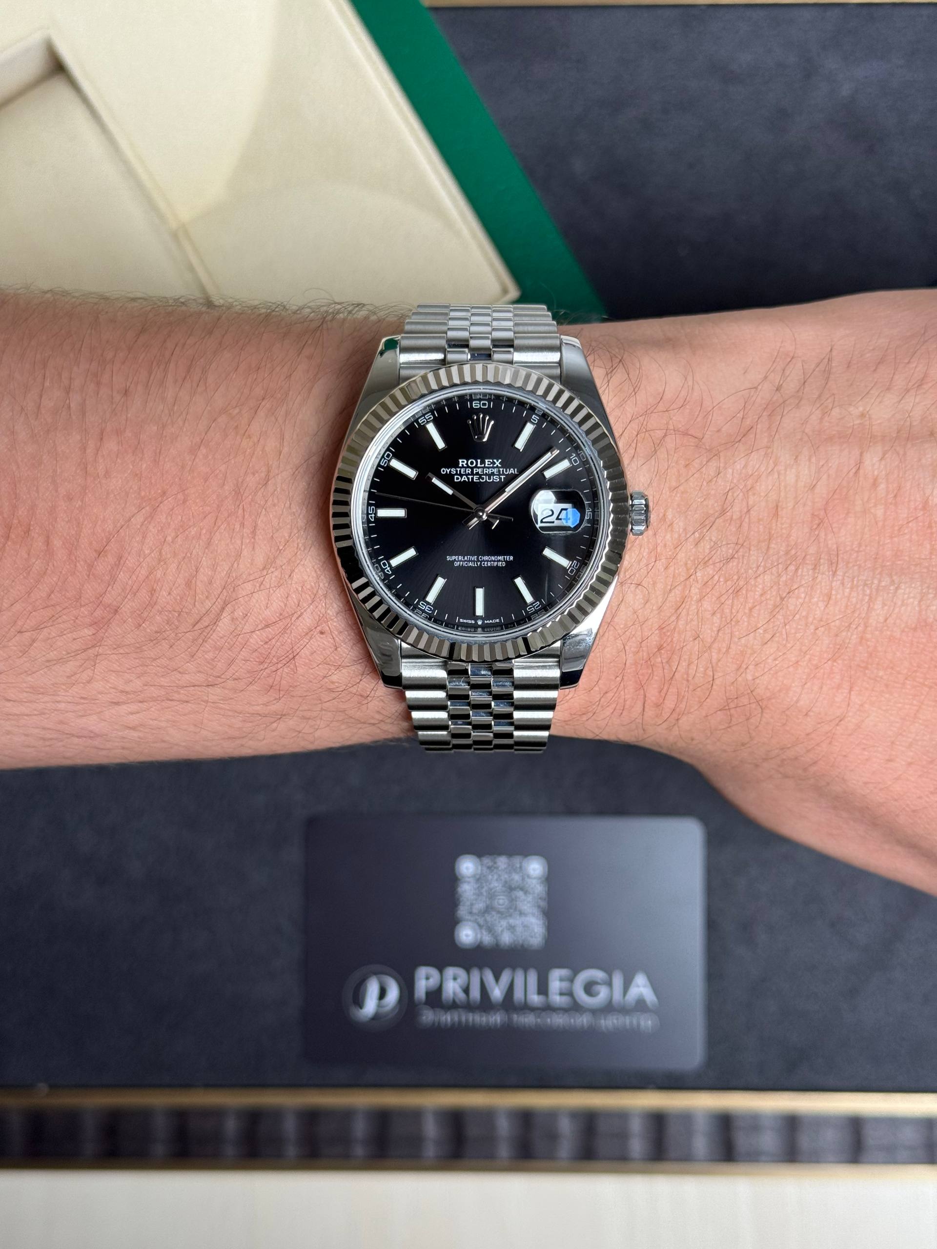 Close-up of a stainless steel Rolex watch on a wrist, featuring a black dial, fluted bezel, and Jubilee bracelet.