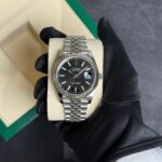 Close-up of a stainless steel Rolex Datejust watch on a beige display cushion, held by a gloved hand; black dial with silver markers and fluted bezel.