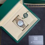Open green Rolex box with a two-tone watch resting in a beige insert and a green seal tag nearby.