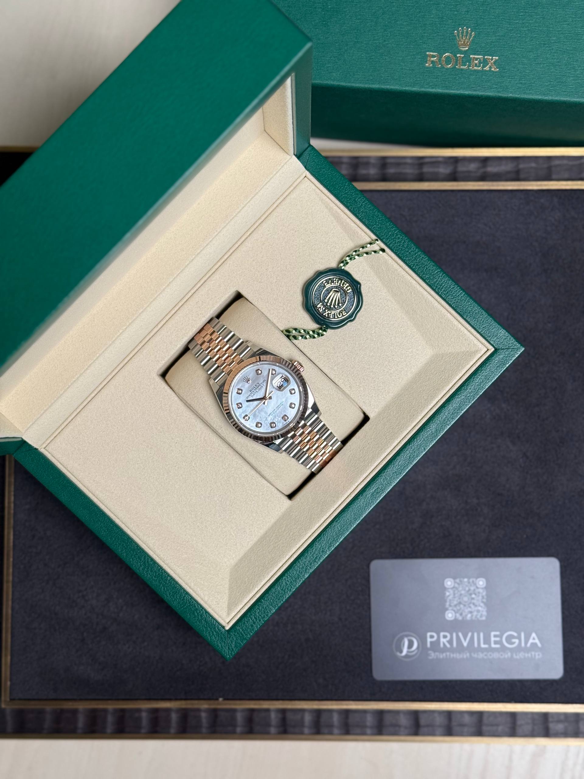 Open green Rolex box with a two-tone watch resting in a beige insert and a green seal tag nearby.